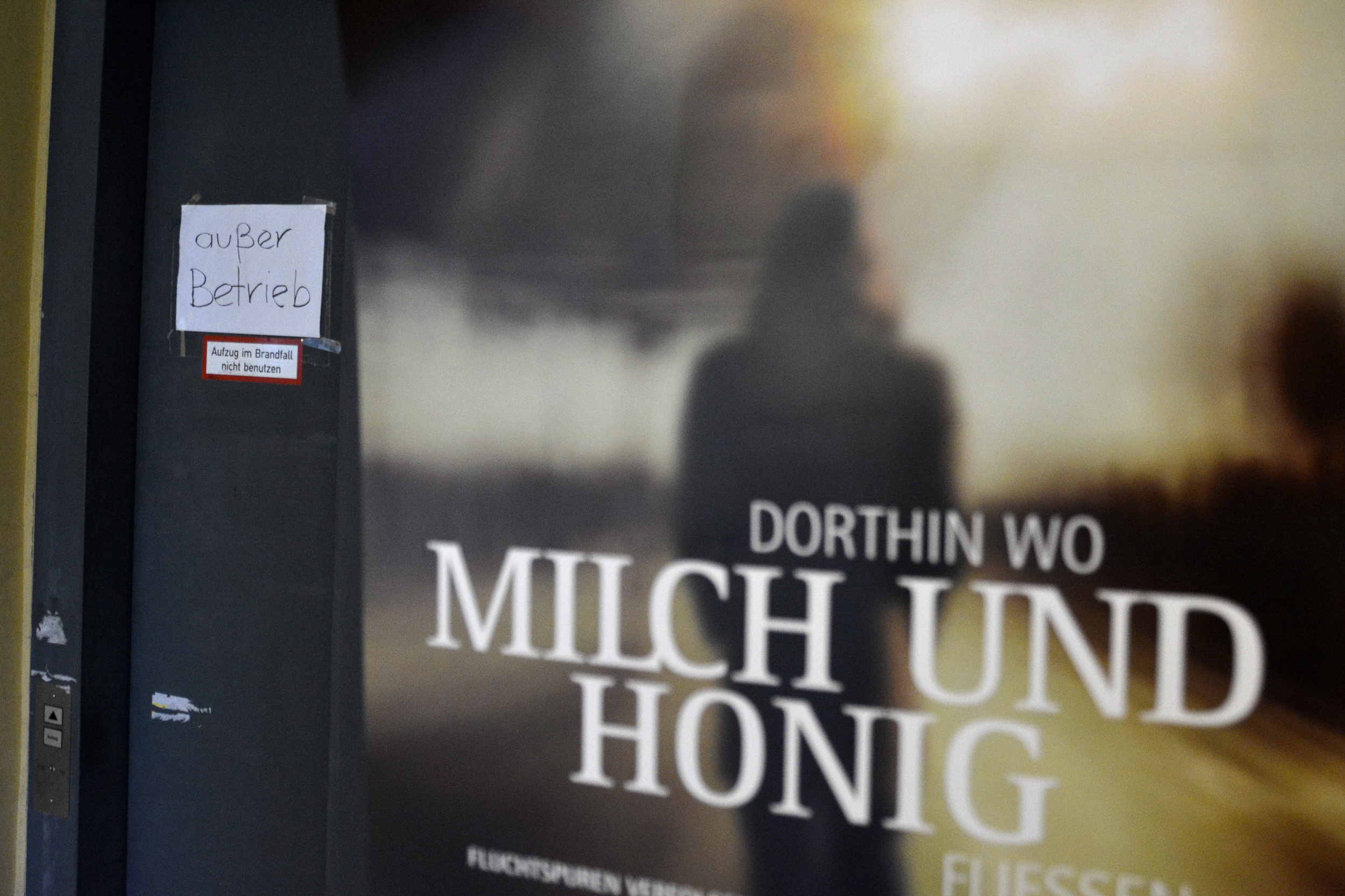 Schild "außer Betrieb" am Aufzug im Parkhaus, davor Plakat zu "Dorthin wo Milch und Honig fließen". Foto: Vera Lisakowski