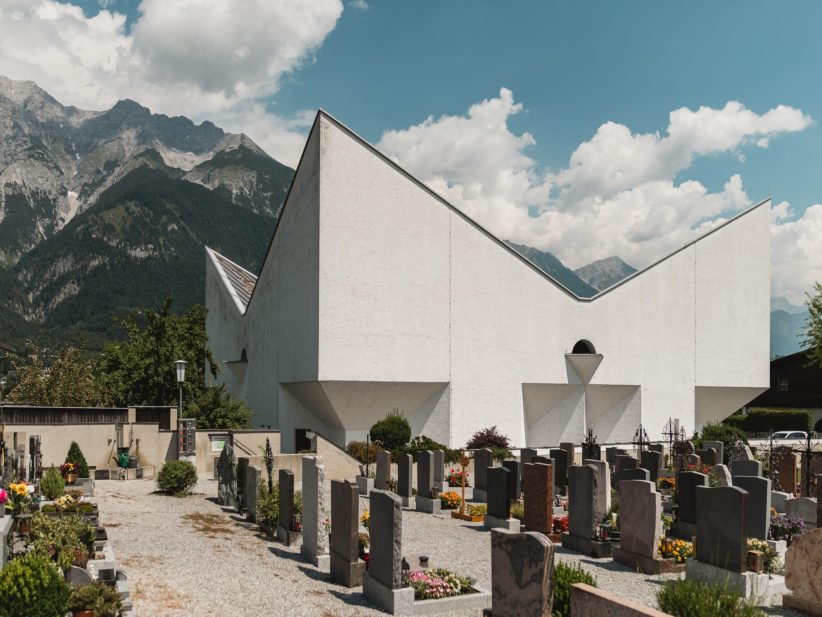 Helle Kirche mit steil gezacktem Dach vor Bergen. Foto: Gregor Zoyzoyla